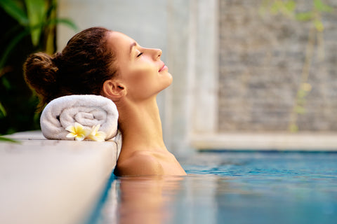 Woman relaxing at spa pool in the bath with head leaned back on a towel and hair tied up