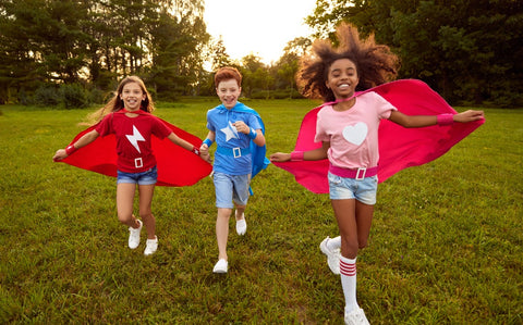 Due ragazze e un ragazzo vestiti da supereroi che corrono per il parco.