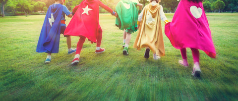 5 bambini vestiti da supereroi che corrono per il parco
