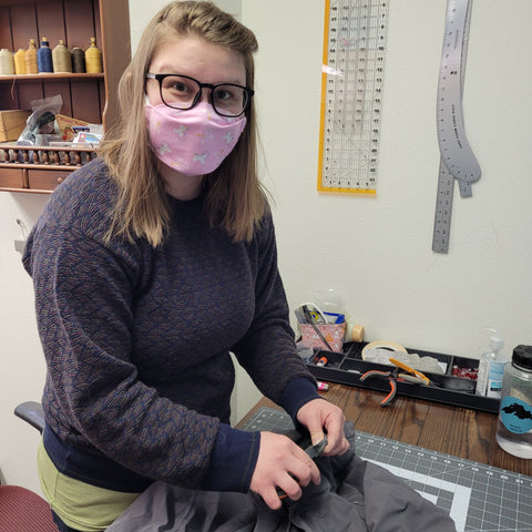 Fran smiling in her Unicorns in Space Mask working on mending a customer's jacket