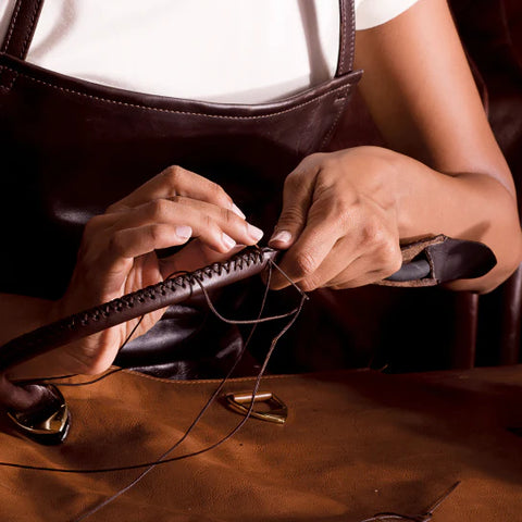 person hand stitching a leather bag