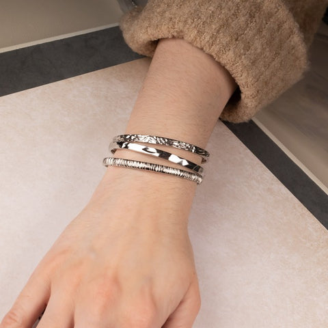 A model's wrist showing three silver bangles of different textures
