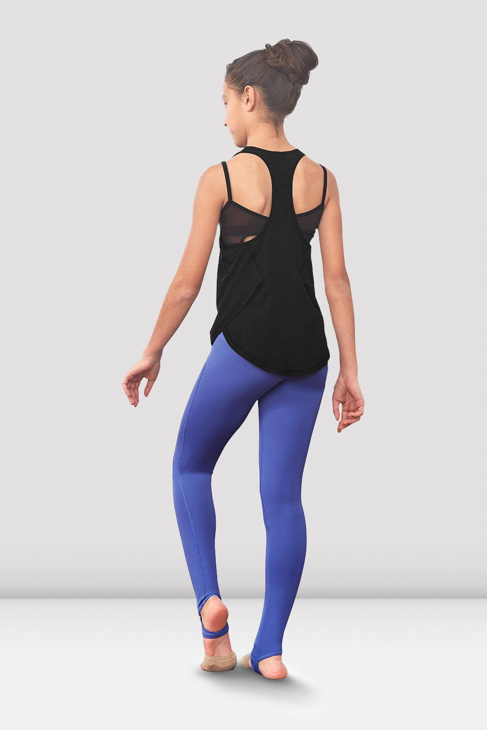 A young dancer wearing the Girls Niomi racerback tank top with stirrup leggings in Iris