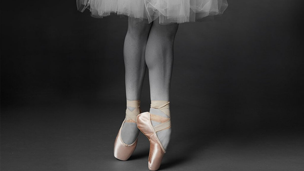 A ballet dancer en pointe wearin pink pointe shoes and a white tutu