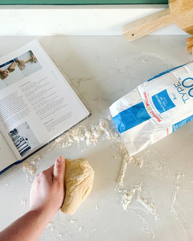 hand kneading dough with a bag of flour on the table and recipe for pasta from scratch 