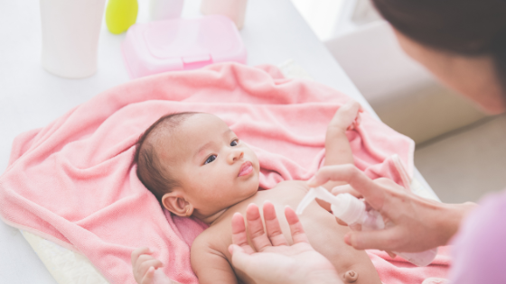 a baby lays on a pink blanket getting lotion put on its skin as its parents navigate how to treat eczema without steroiods