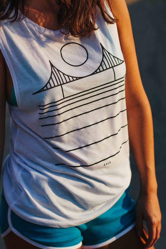 A close up of a girl wearing a white golden gate bridge muscle tank top while the sun sets.