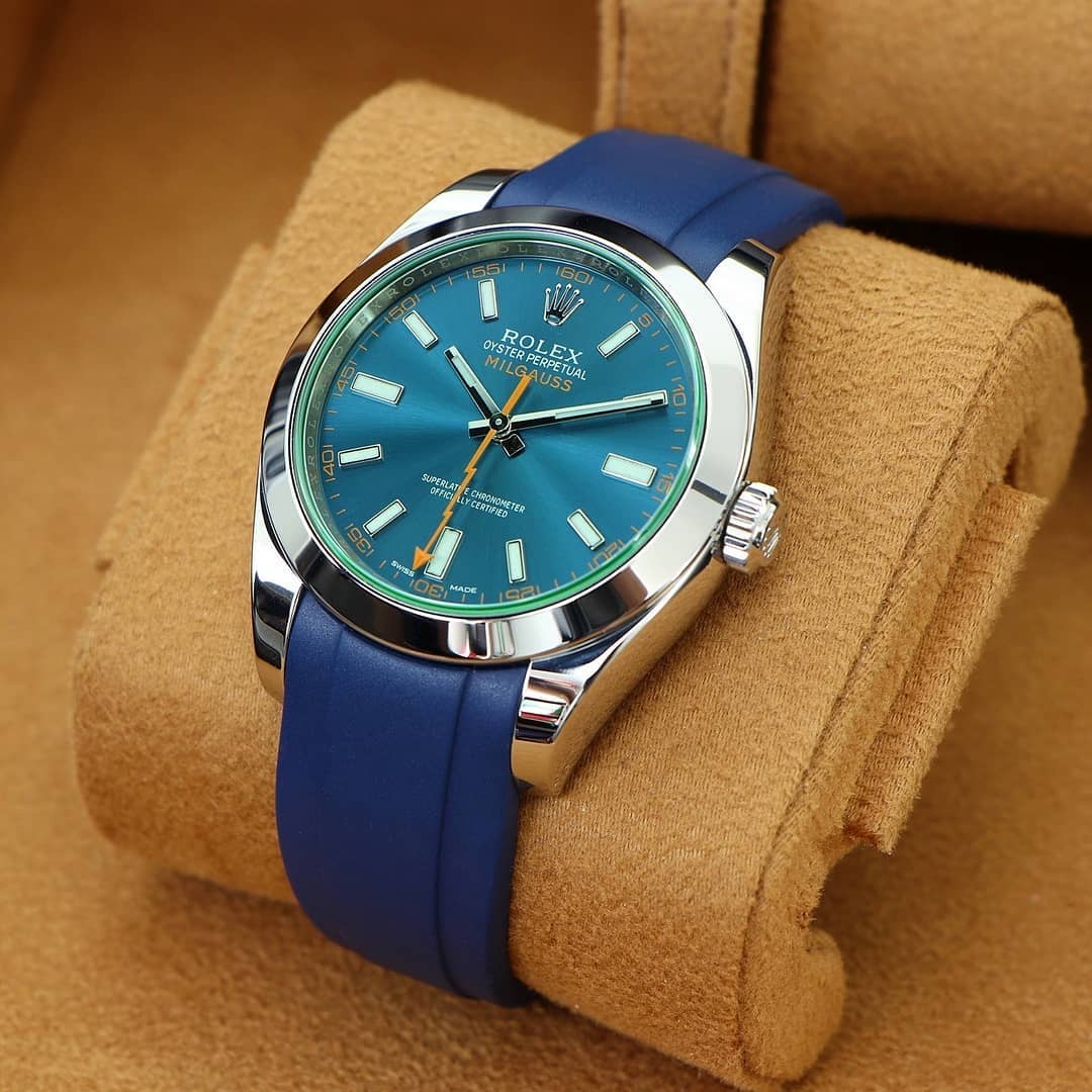 rolex milgauss watch on a blue rubber strap buckled around a tan colored watch pillow