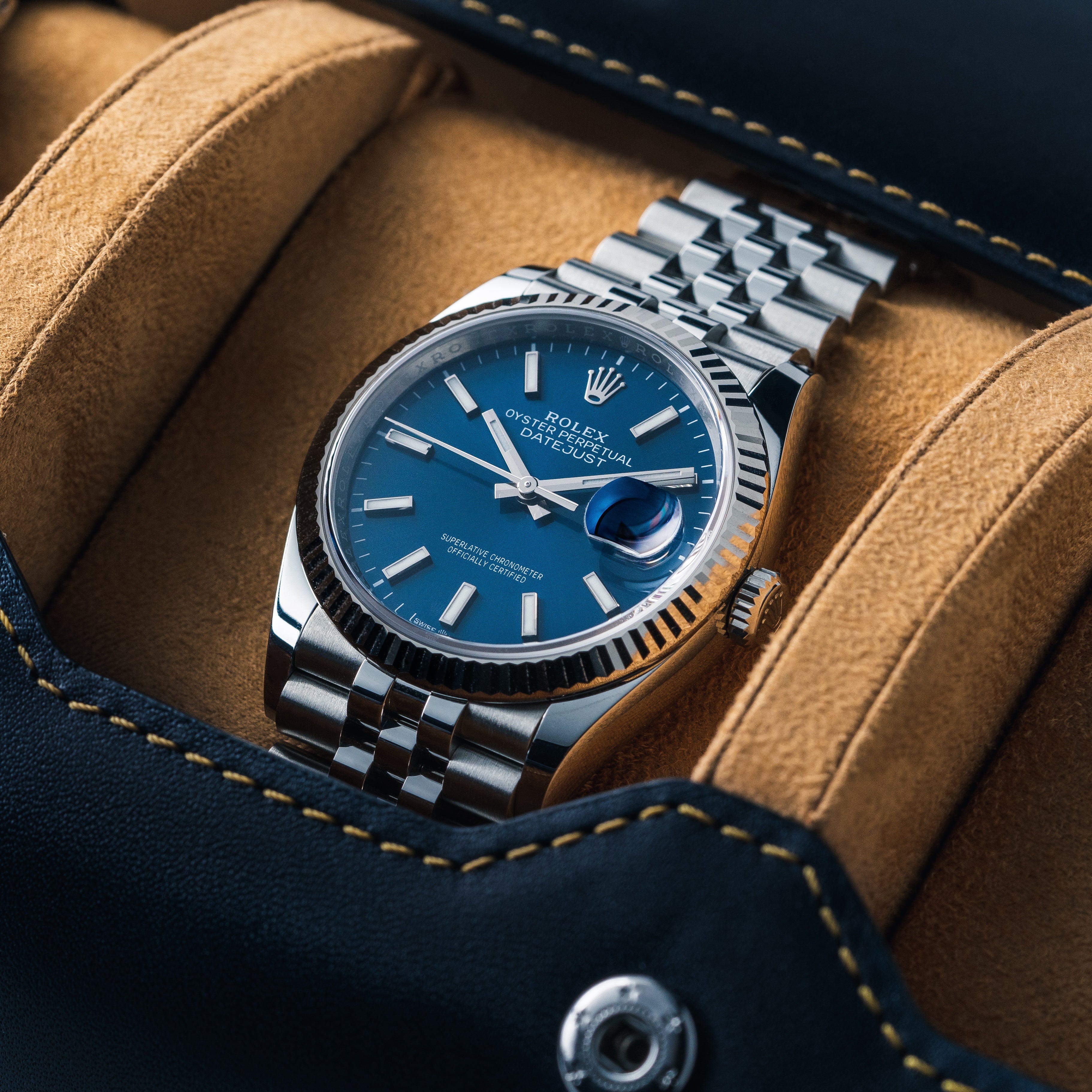 rolex datejust watch with blue dial resting on a tan microfiber insert inside of a blue leather watch roll