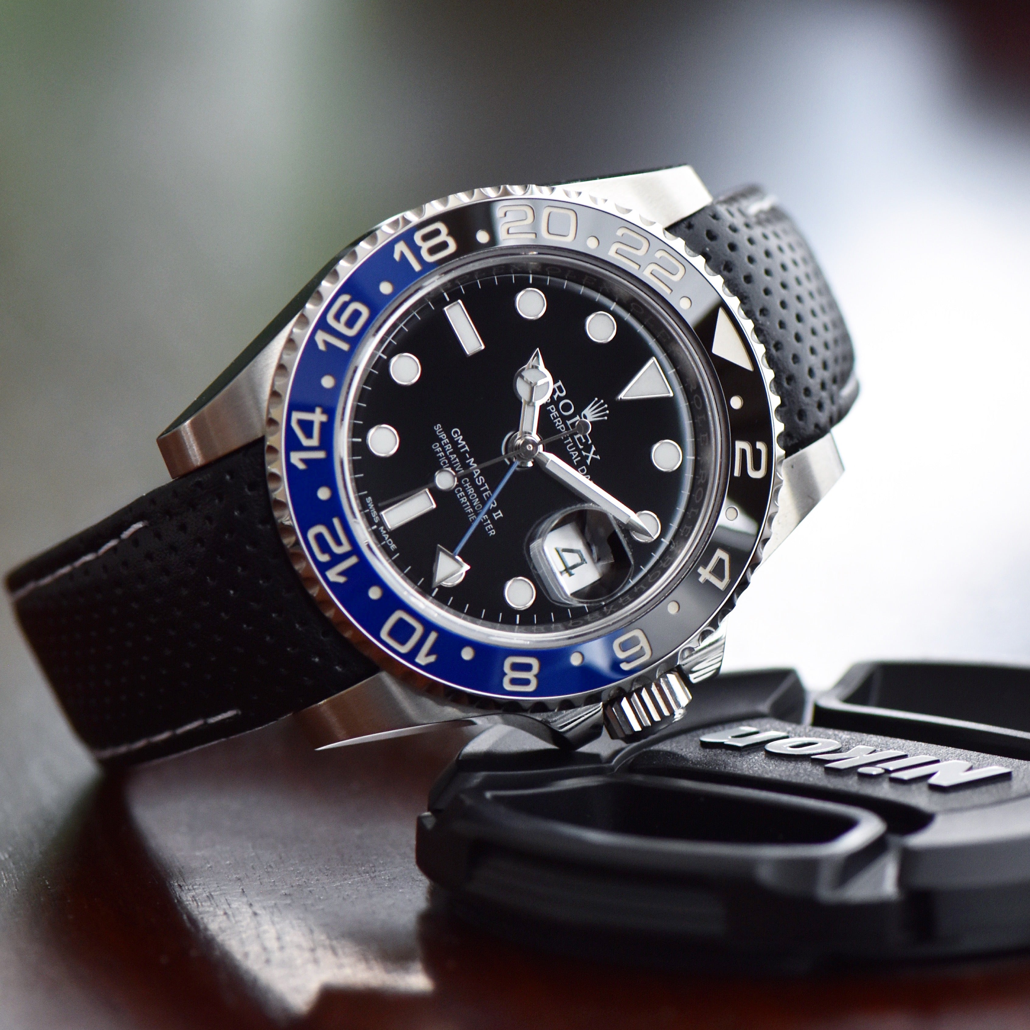 rolex gmt watch with bi-color blue and black bezel with a perforated leather watch strap on it, resting on top of a car key fob