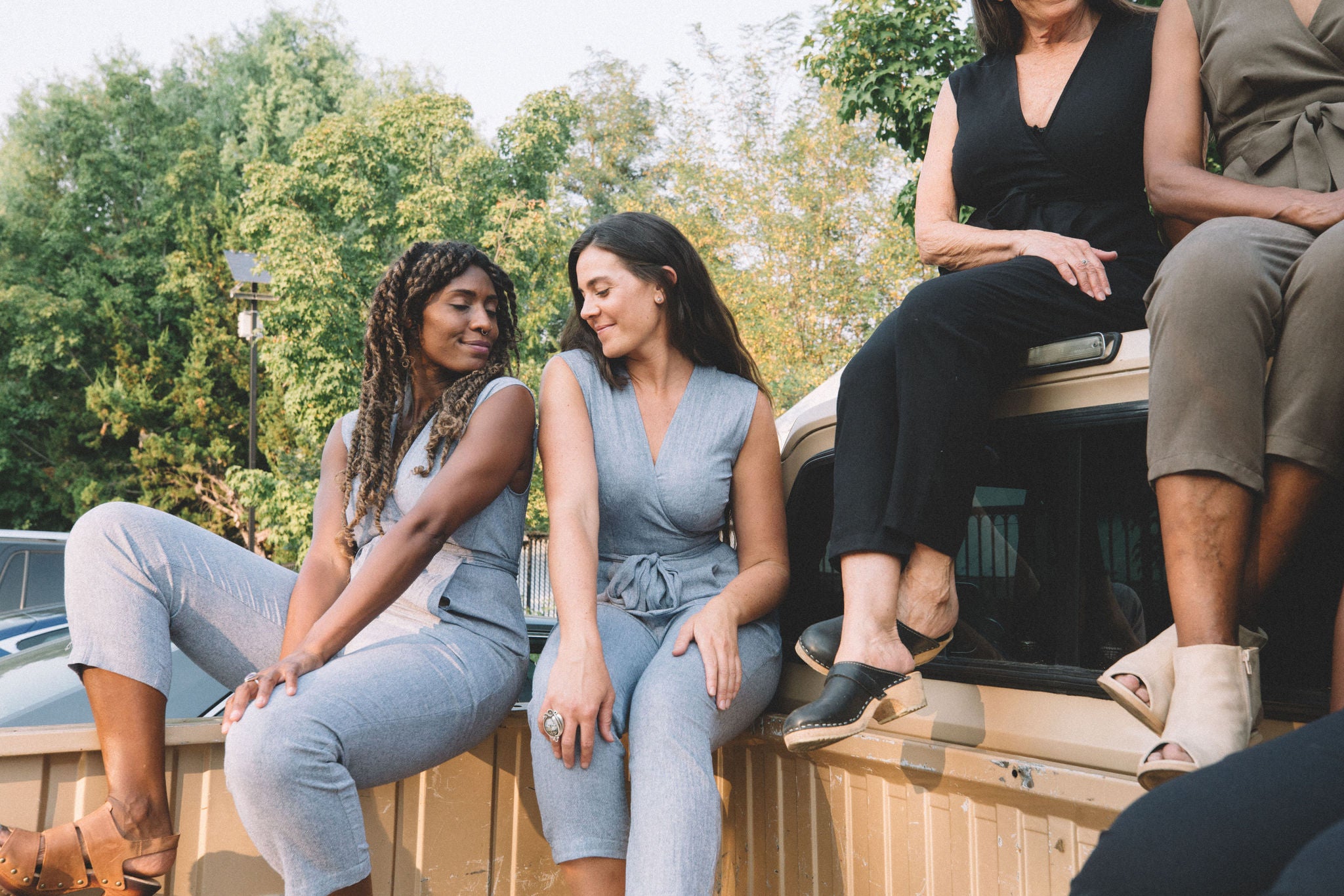 women sitting in the back of a truck with high waisted jumpsuits on 