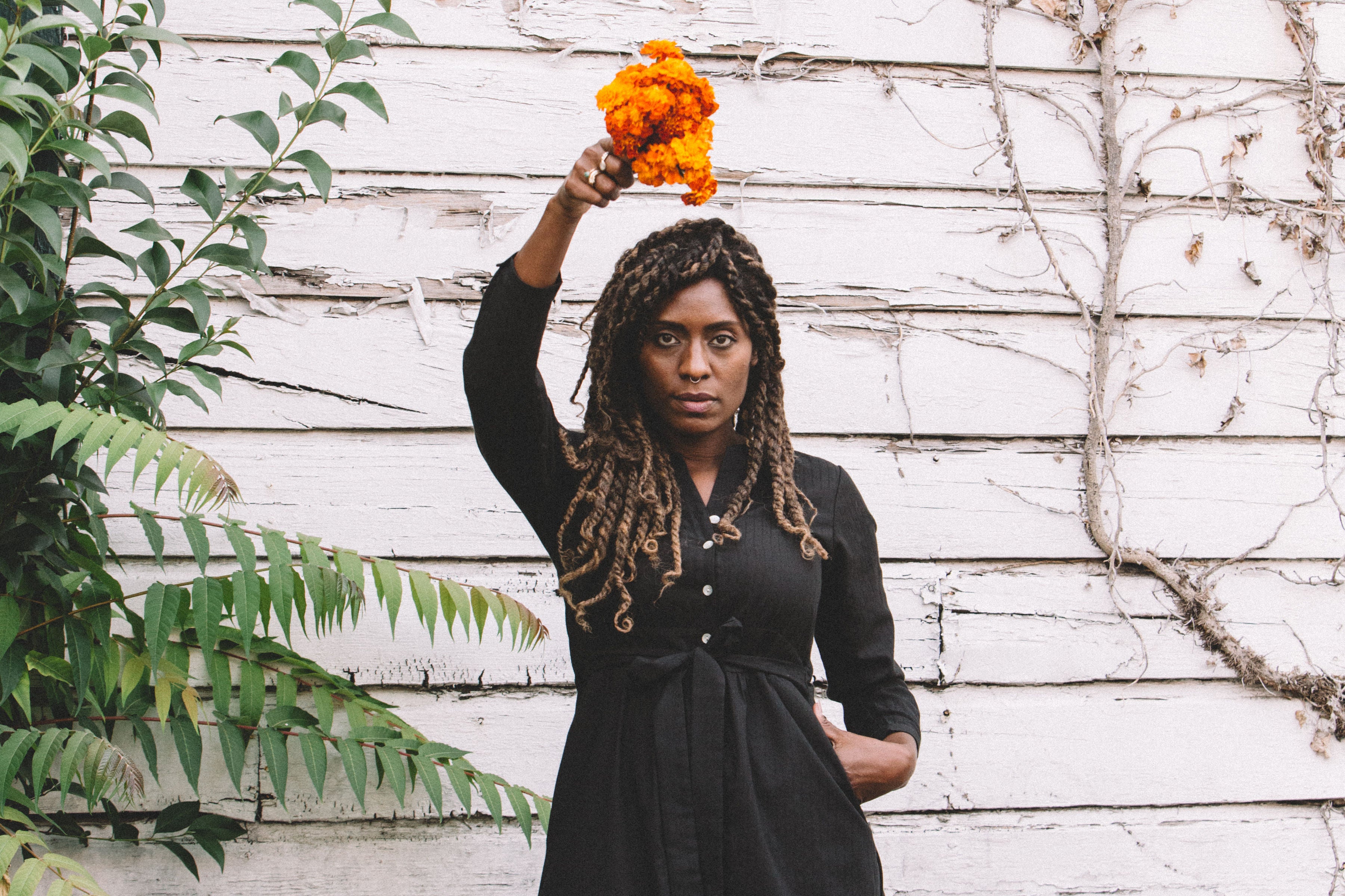 black woman in long black dress with a marigold flower over her head 