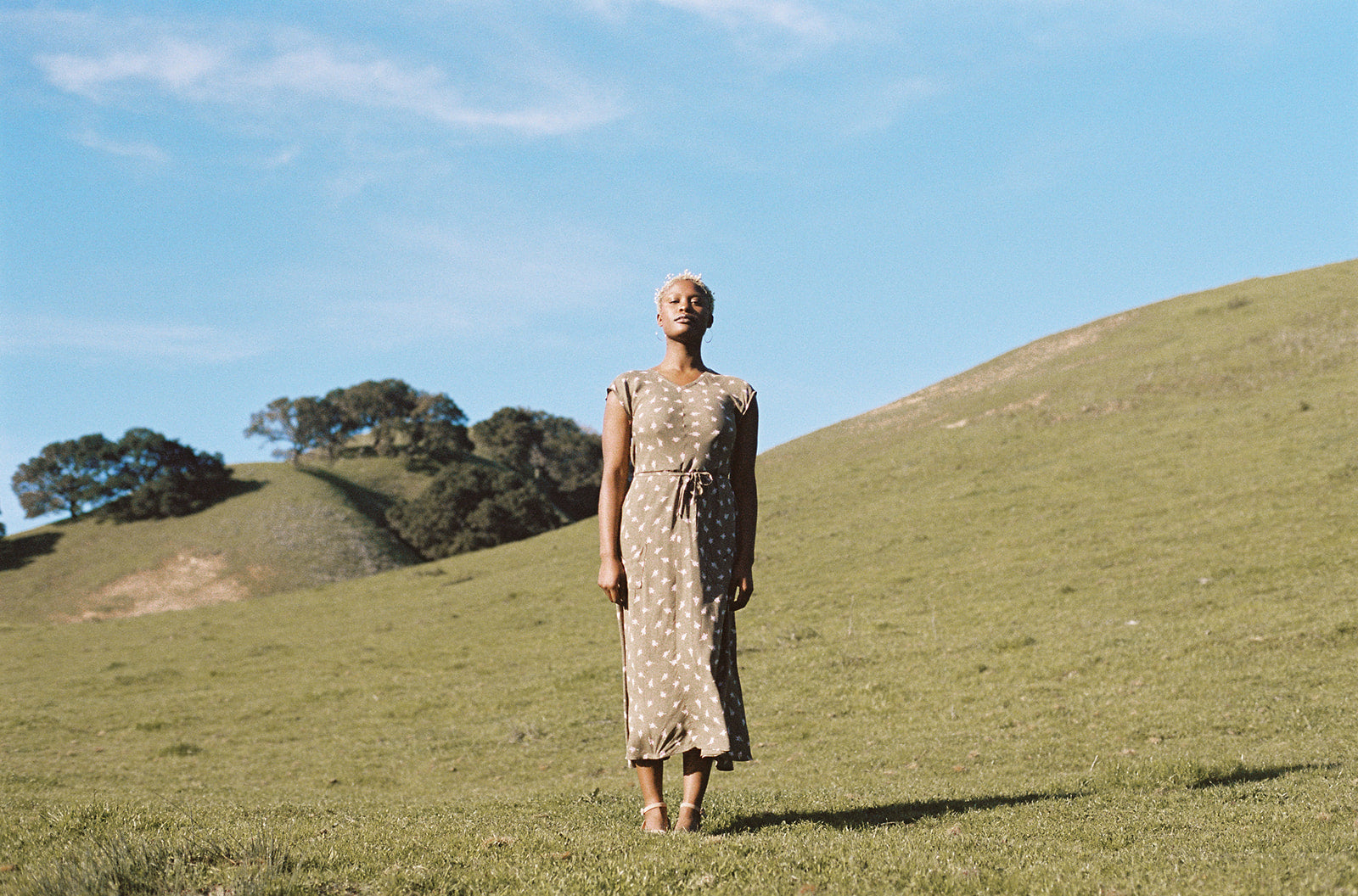 black woman wearing a olive dress on a hill top 