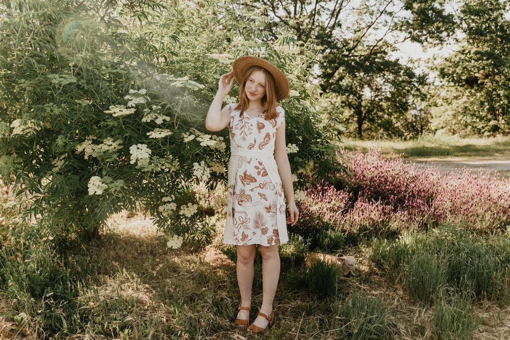 woman wearing a brown and white pinafore dress with a sun hat 