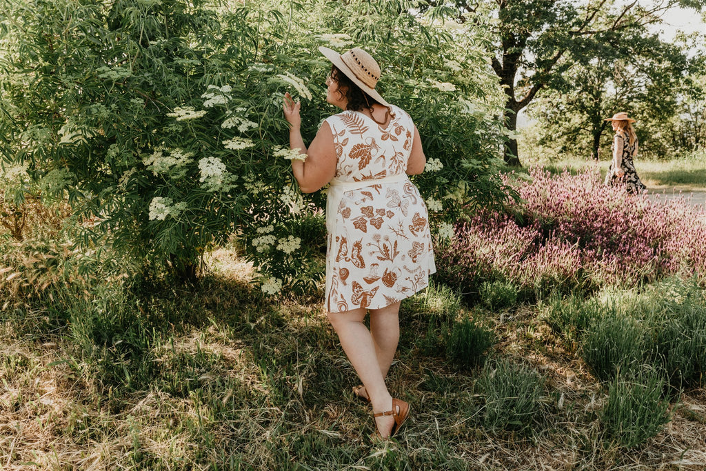 plus size woman wearing a brown and white pinafore dress with sun hat 