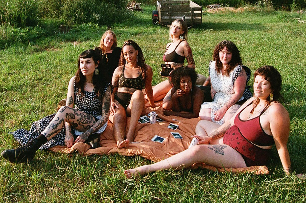 collaboration of women designers in a field on a blanket wearing eachothers designs 