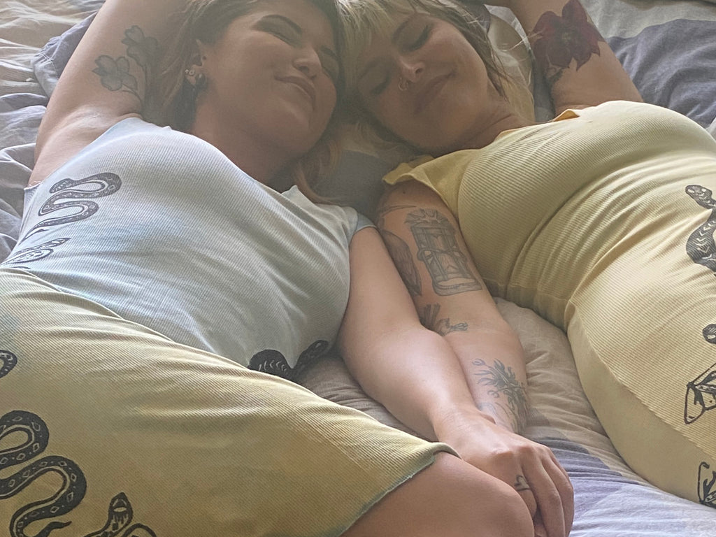 sisters laying in a bed together wearing plant dyed organic cotton dresses with snakes printed on them 