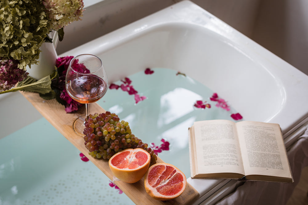 Badewannenbrett mit Wein, einem Buch und Obst