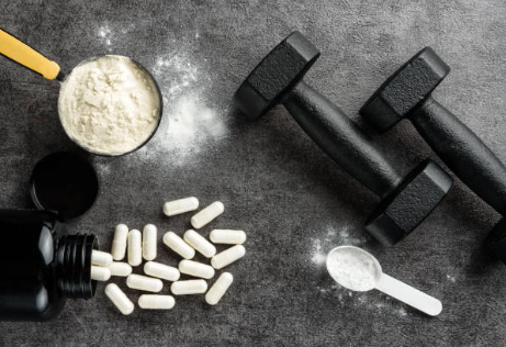 Weight handles alongside a selection of supplement pills and a scoop filled with pre-workout powder.