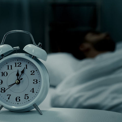 alarm clock next to a bed with someone sleeping