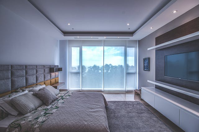 Chambre avec une télévision en face du lit avec jeté de canapé gris