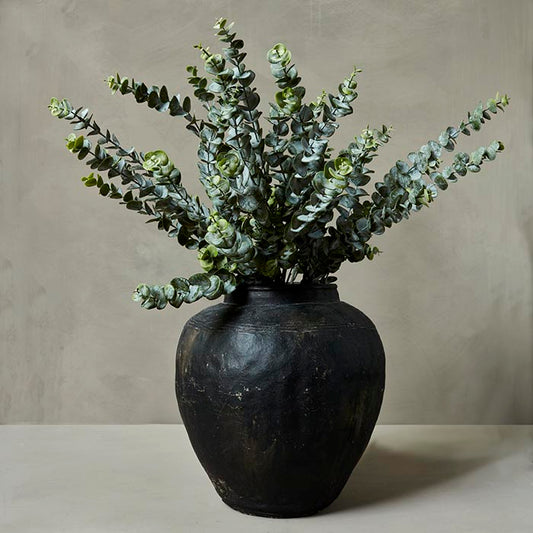 Artificial eucalyptus foliage stems inside a black stoneware vase.