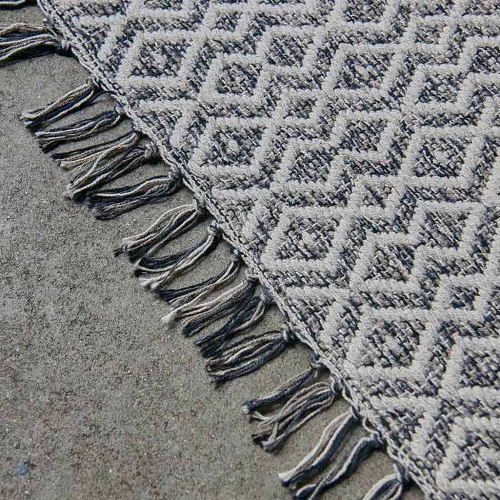 Mixed grey and white tasseled edge of a diamond pattern rug