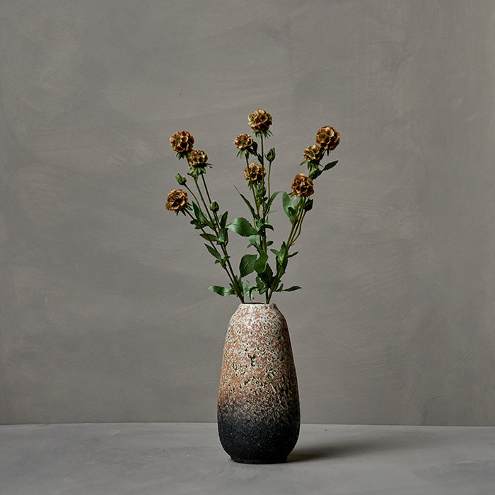 Artificial scabious seed pods in a ceramic vase.