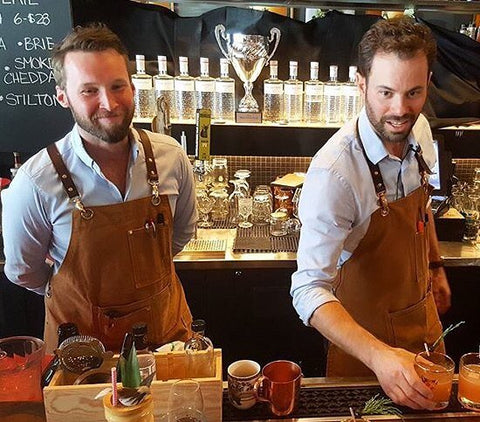 Two bartenders wearing luxury bartender aprons made from brown canvas. Search & Rescue Denim Co makes high-end, high-quality bartender aprons.
