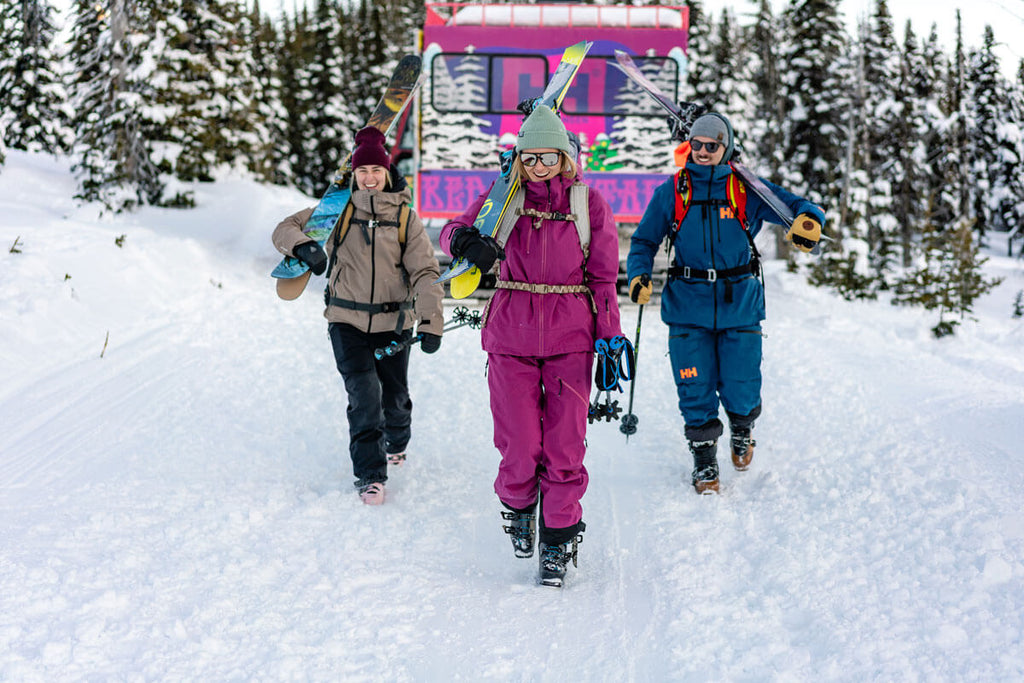 group of skiers walking away from a snow cat carrying equipment