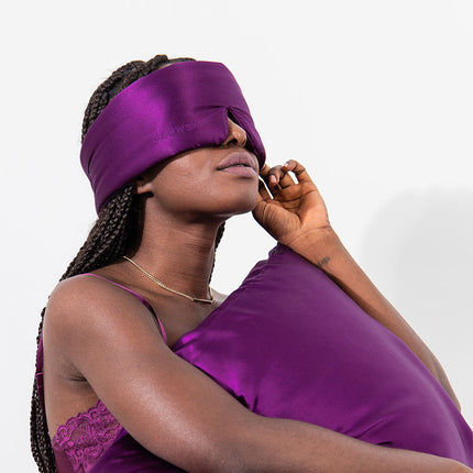 Model putting on purple Drowsy silk sleep mask with a white background