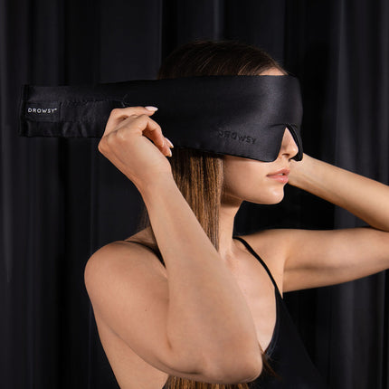 Model putting on black Drowsy silk sleep mask with a black background