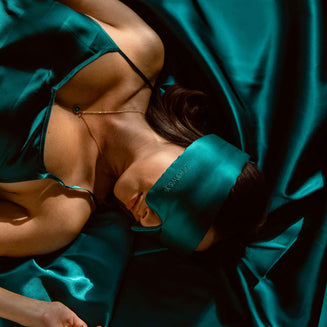 Model sleeping on green silk with a Drowsy green silk sleep mask covering her eyes