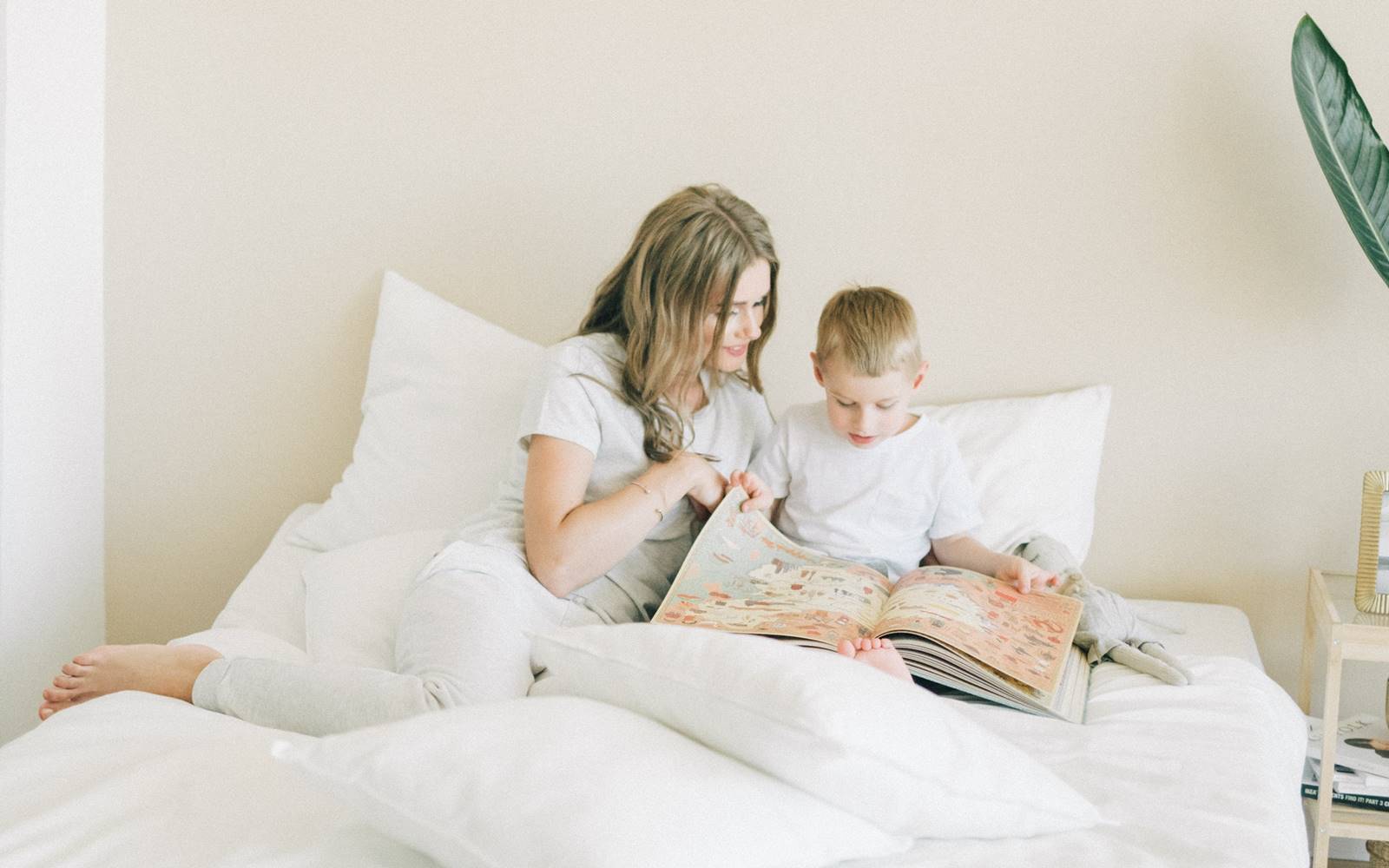 一个男孩在铺着白床单的床上给他妈妈读书。