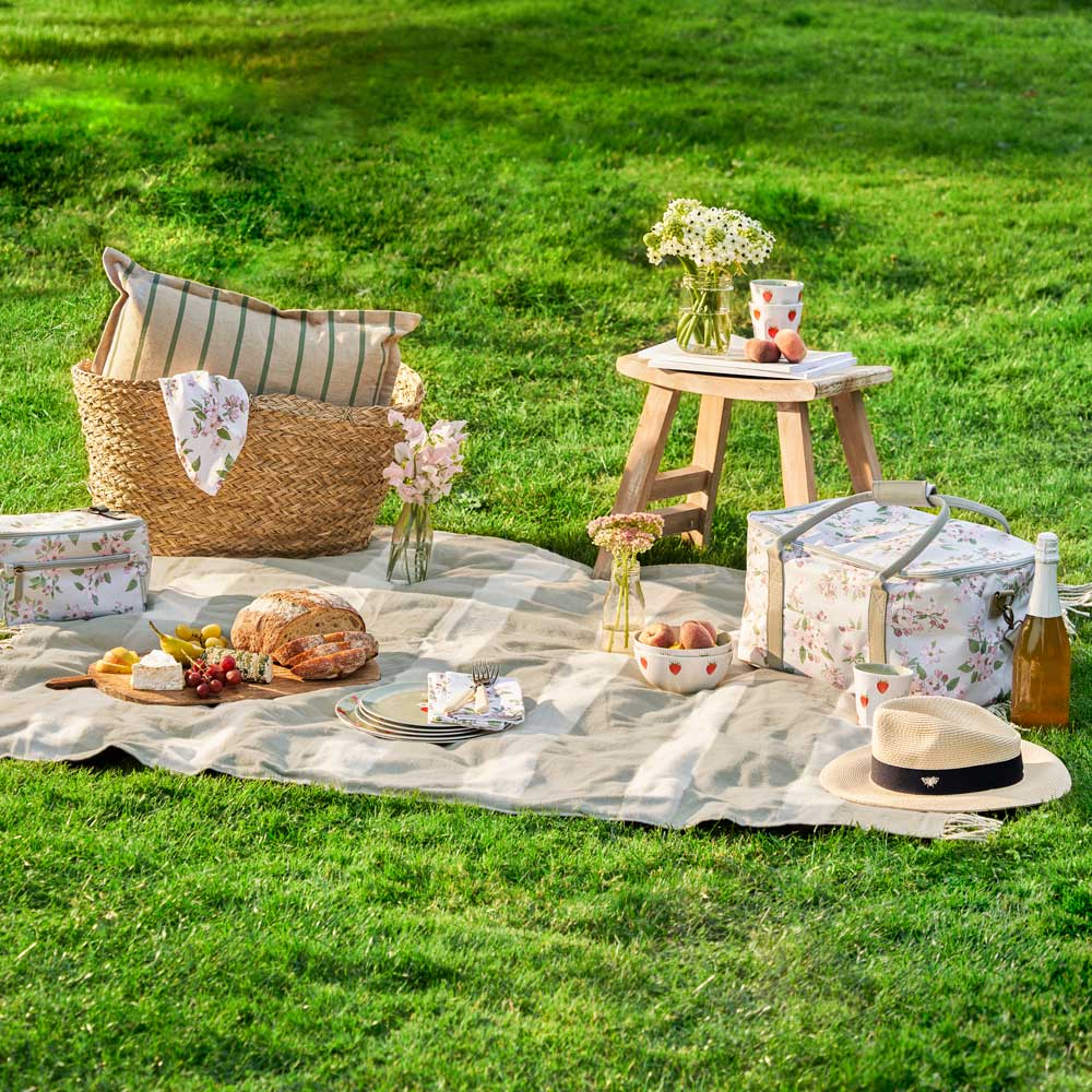 Gingham olive green picnic blanket with floral blossom picnic bag and range of melamine set up in the park