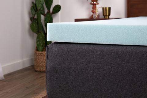 An up close photo of a gray mattress with a blue memory foam mattress topper on top of it.