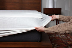 Hands stretching protector skirt over mattress