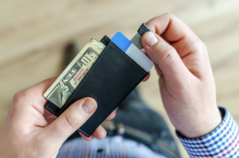 A photo of a man holding his wallet that has $10 sticking out of it