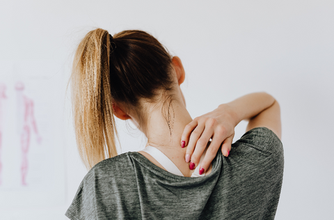 A woman reaching behind her back and holding her neck like it's in pain