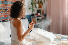 A woman sitting on her bed a spraying a room refresher spray