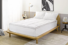 Photo of a bed with a quilted white mattress topper fitted over the mattress.