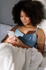 A woman relaxing in bed while using her cell phone.