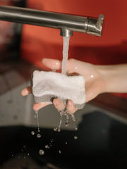 Photo of a person holding a sponge underneath a running faucet