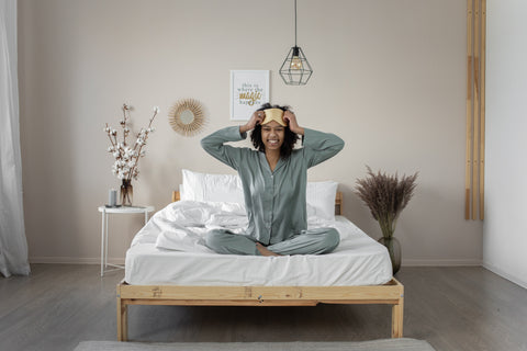A woman wearing pajamas and smiling while sitting on a bed with white bedding.