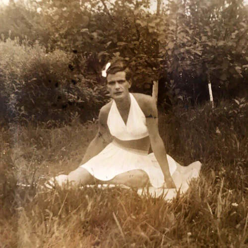 Person dressed as woman in skirt and halter top sitting on grass