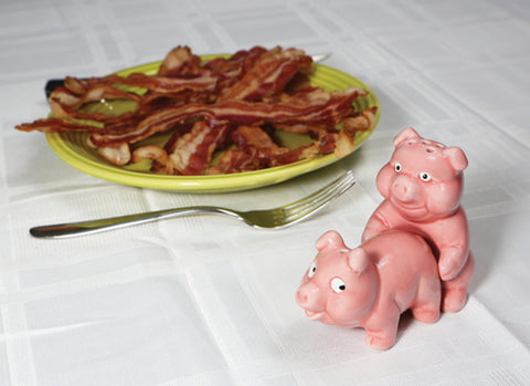 Pig salt and pepper shaker set on a table beside a plate of bacon