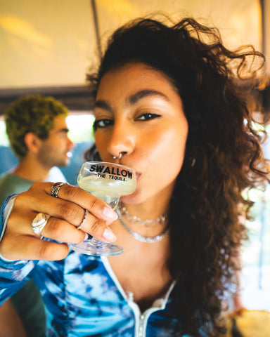 Girl with brown, curly hair drinking from a shot glass