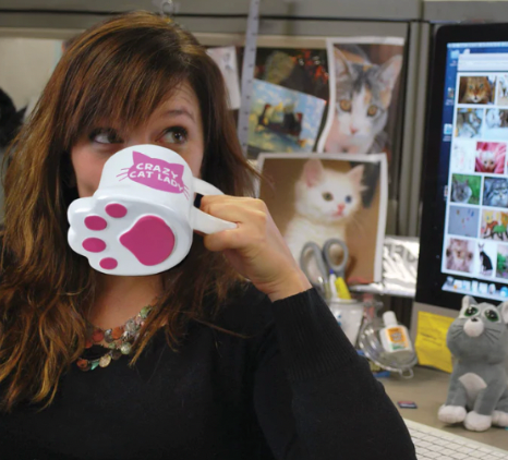 Woman drinking from a mug shaped like a cat's paw that says Crazy Cat Lady on the front