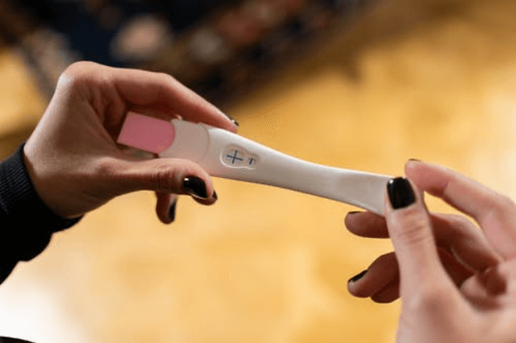 woman's hands holding a positive pregnancy wand