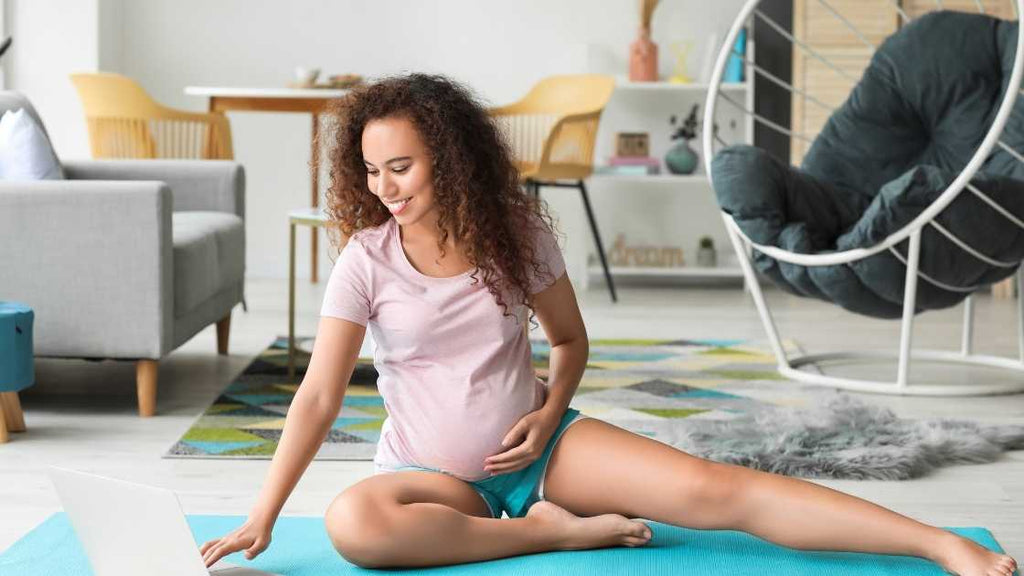 pregnant woman on floor at home reading SpeciallyMe's workout routines on laptop